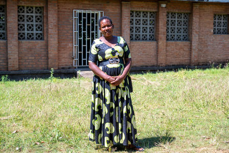 Woman standing on grass in front of a brick building, wearing a black-and-lime patterned dress.