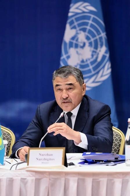 Photo: Man in suit speaks at conference; UN flag backdrop.