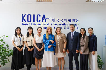 Diverse group of eight professionals posing in an office lobby beside a KOICA sign.