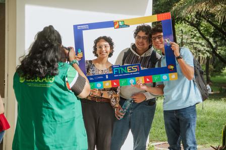 Group of people outdoors, smiling, posing with a blue photo frame prop decorated with icons.