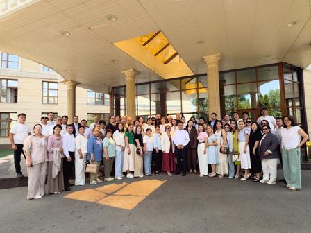 Large group of people in semi-formal attire posing outside a modern building entrance.