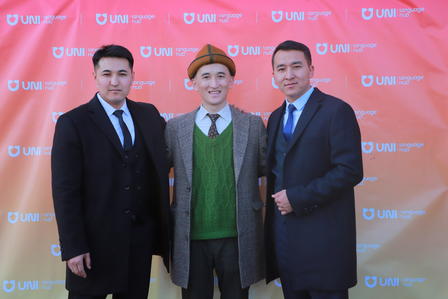 Three men in suits posing in front of a colorful backdrop with repeating logos.