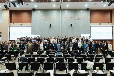 Group of attendees posing for a photo in a conference hall with empty chairs in the foreground.