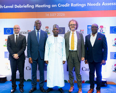 Group photo: six men in suits and one in a white robe on stage at a credit ratings conference.