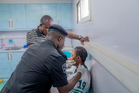 Photograph of a barber in a cap cutting a young boy's hair as another man watches.
