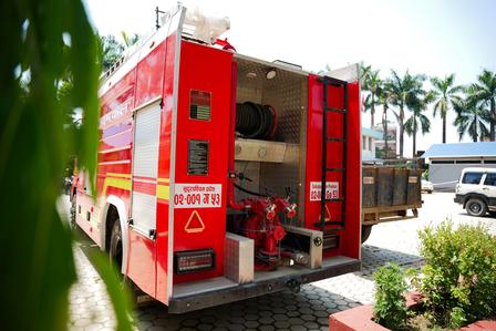 Red fire engine with open rear doors and visible equipment, parked near palm trees in a sunny lot.