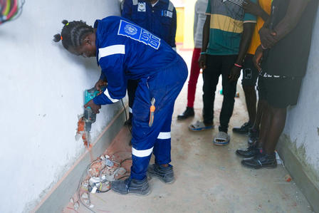 Photograph: worker in blue coveralls patches a wall while onlookers watch.