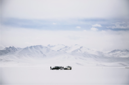 Photograph of a small group on a vast snowy plain with distant snow-capped mountains.