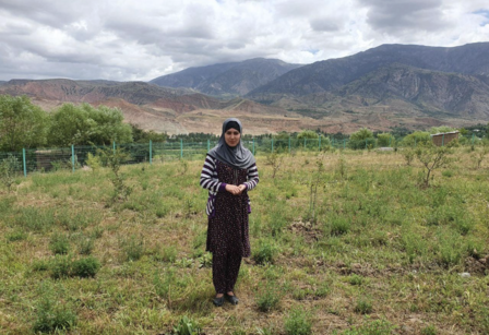 Photograph of a person standing in a grassy field with distant mountains.