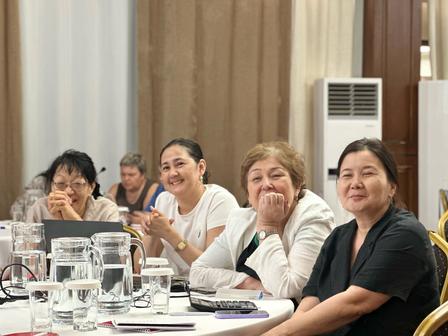 Five women seated at a white-tablecloth dining table, smiling with drinks.
