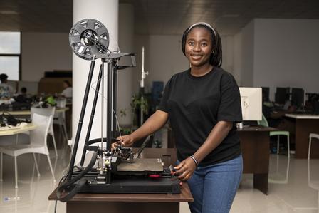 Photograph of a smiling woman in a black shirt beside a tall lab machine on a workbench.