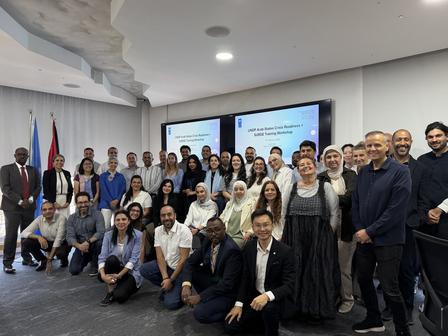 Group photo of attendees in a conference room with flags and a presentation screen.