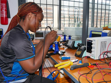 Person soldering at a lab bench with electronics components and tools.