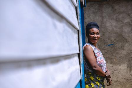 Photograph of a smiling woman in a patterned dress standing beside a blue wall.