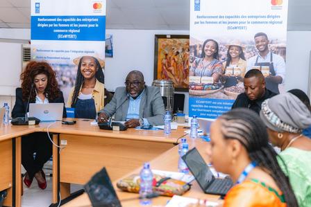 Diverse group at a conference table with laptops; banners in the background.
