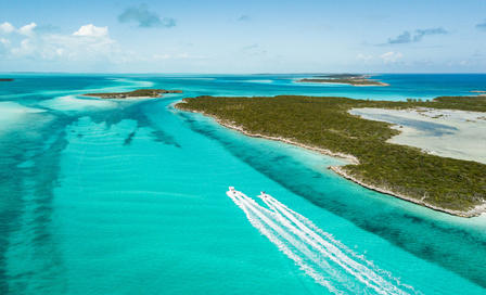 Aerial view of a turquoise lagoon with white sandbars, mangroves and a boat wake.
