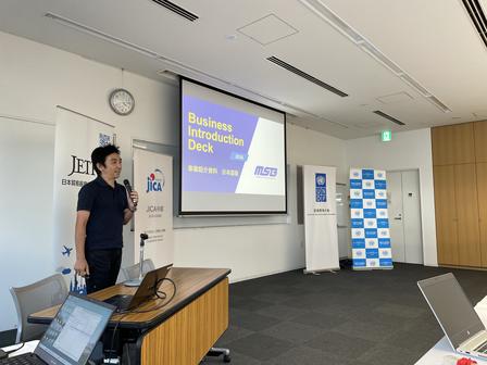 Man presenting beside projected slide in a bright conference room.