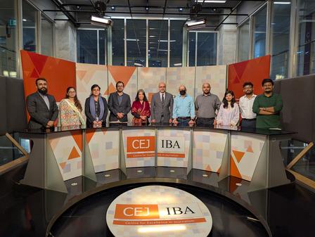 Photo of professionals standing behind a curved desk with CEI IBA logos in a colorful studio.