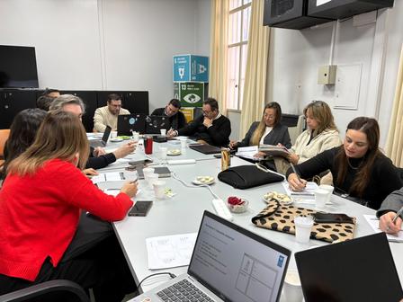 Group of people around a conference table in a meeting room with laptops, papers, and snacks.