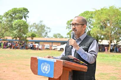 Speaker at podium with UN emblem, addressing crowd at outdoor event.