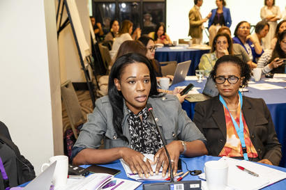 Two women panelists at a conference table with papers and microphones, addressing an audience.
