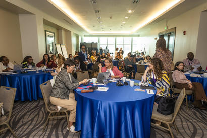Group of professionals at round tables with blue cloths in a bright conference room.