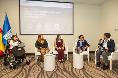 Panelists sit on stage in a conference room with a projected slide and flag on the left.