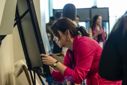 Woman in pink leaning to use a touchscreen kiosk in a busy store.