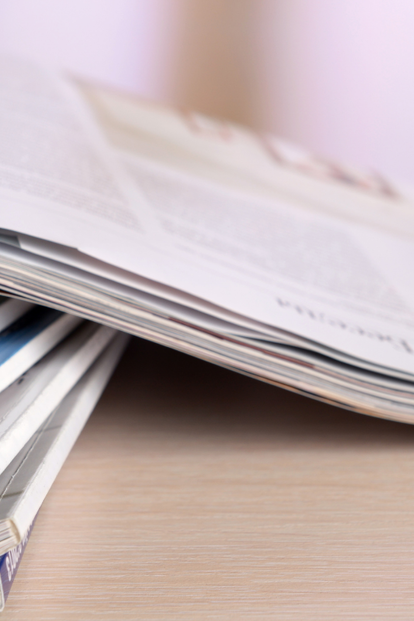 Stack of magazines with pages fanned open on a wooden table.