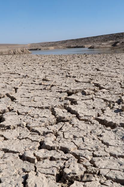 Cracked dry earth desert landscape with distant hills under a clear blue sky.