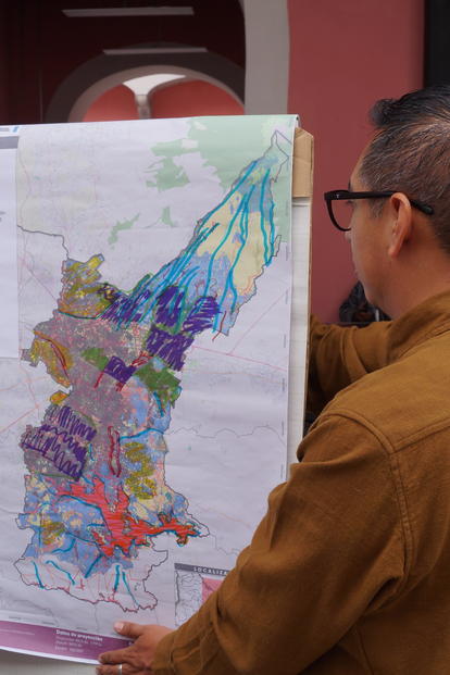 Two people hold a large colorful map outdoors, in front of a red building.