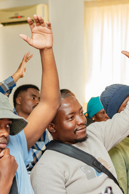 Attendees in a bright indoor space raise their hands.