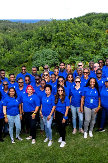 Group portrait of people in blue shirts posing on a grassy field outdoors.