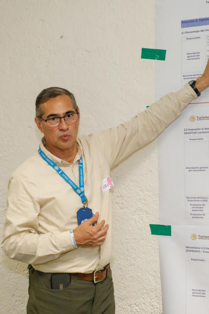Photograph of a presenter with a microphone pointing at posters during a conference.