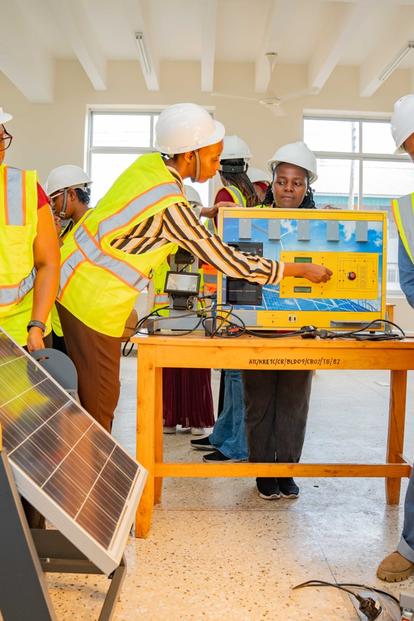 People in hard hats and safety vests inspect a blue and yellow device on a table in a workshop.