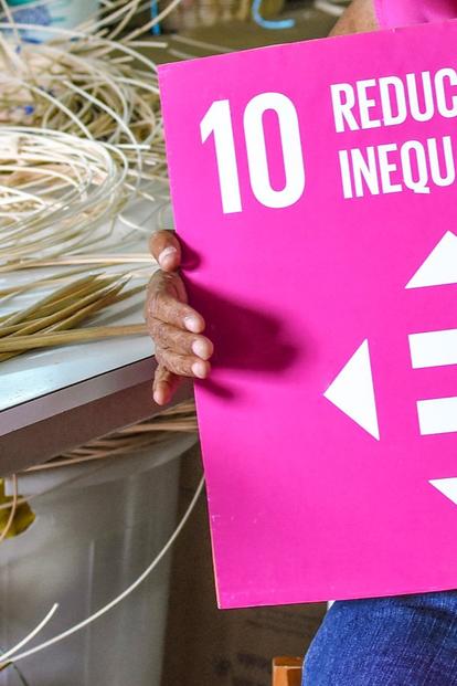 Person in a craft workshop holding a bright pink SDG 10 Reduced Inequalities sign.