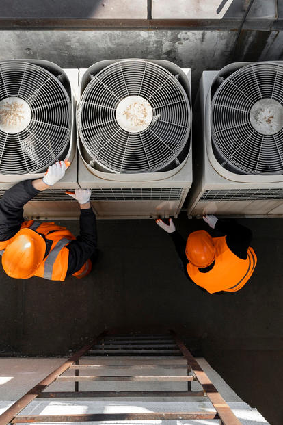 Three outdoor HVAC condenser units on a rooftop, two workers in orange safety vests nearby.