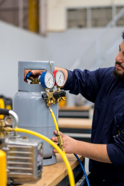 Male technician in blue shirt adjusts a pressure gauge on a yellow machine in a workshop.