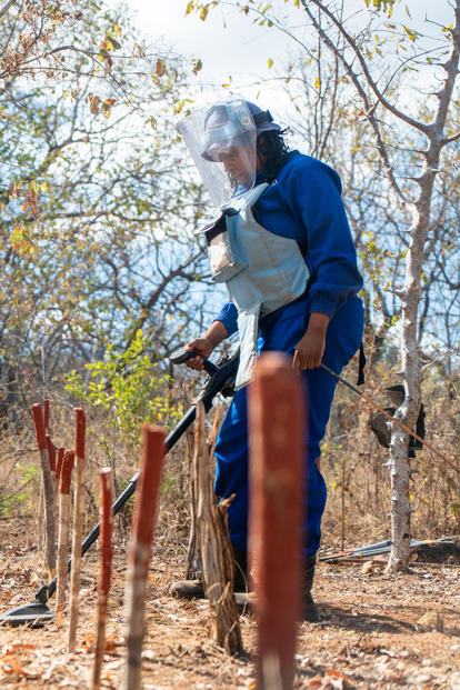 Person in blue coveralls and gloves standing among autumn leaves, working on a fence post.