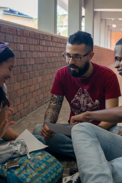 Three students sit on a brick sidewalk, studying together with papers.