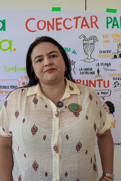 Woman in a light polka-dot blouse standing before Conecta Cartagena posters.