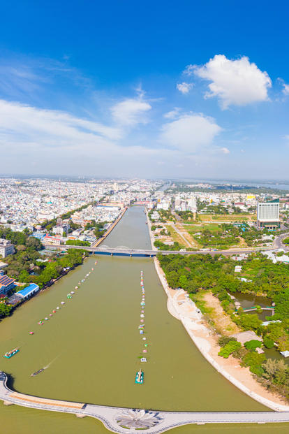 Panoramic aerial view of a coastal town with a river, canal, bridges, and green neighborhoods.