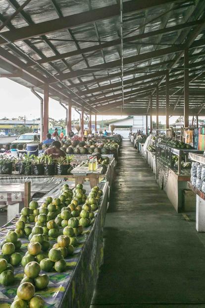 Open-air market with a central water canal and rows of melons under a metal roof.