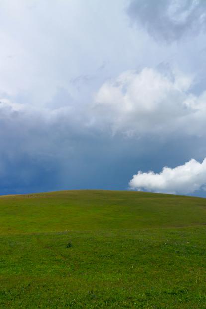 Photo of a green hill under a dramatic cloudy sky.