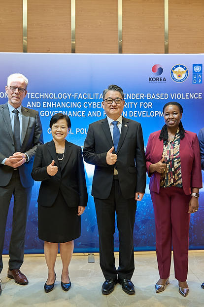 Photo: Eight professionals in formal attire posing with thumbs up in front of a blue backdrop with logos.