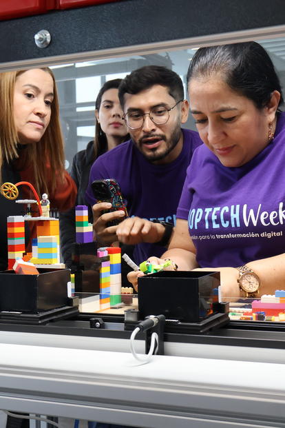 Group of people gathered around a colorful LEGO build on a display table at an event.