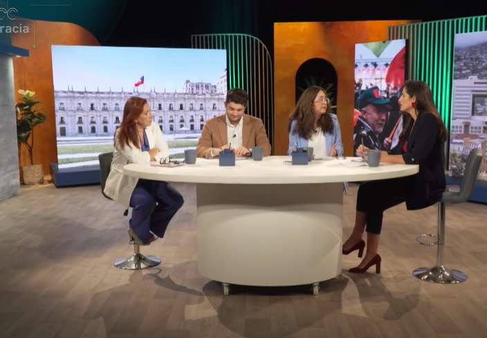 Four people seated at a round table, discussing in a modern studio with colorful backdrops.