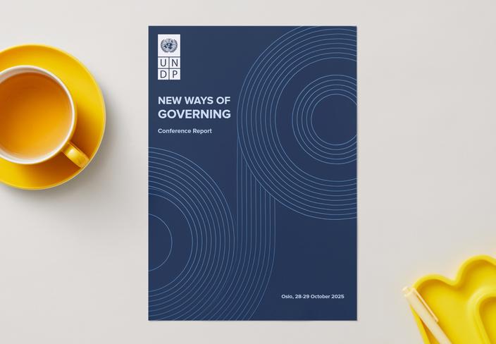 Blue booklet titled 'New Ways of Governing' on a light desk, beside a yellow mug.
