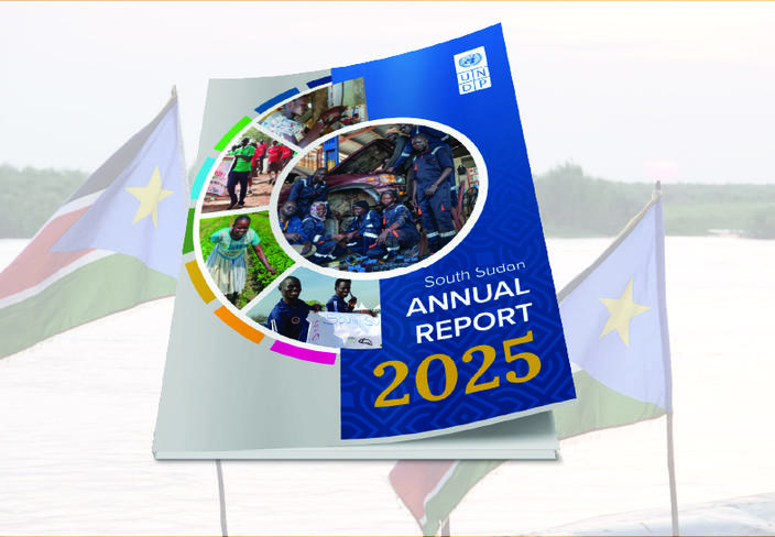 Blue Annual Report 2025 booklet with circular collage on display, flags in background.