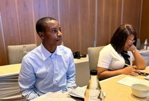 Two individuals seated at a meeting table, one focused and the other using a phone.